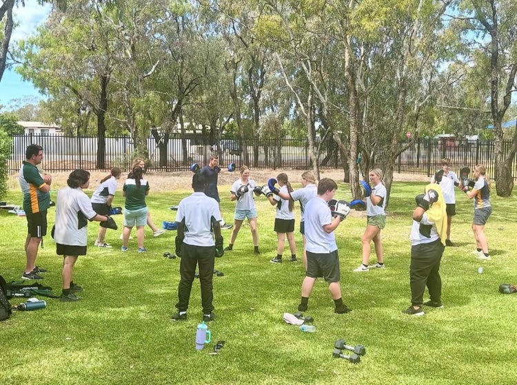 Photograph of students on grassed area surrounded by trees during kickboxing session