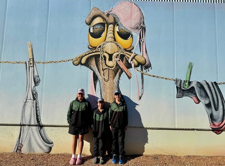 Photograph of students dressed in Wee Waa High School students standing in front of mural of an emu at Lightning Ridge