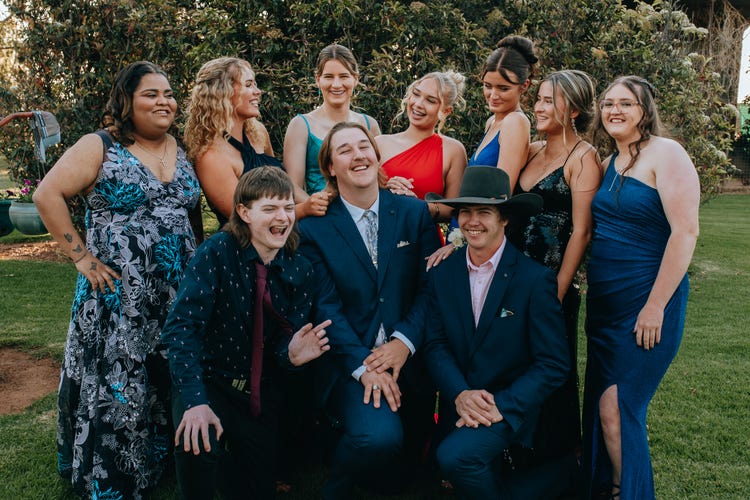 Photograph of students dressed in formal wear smiling and laughing standing on grassed area