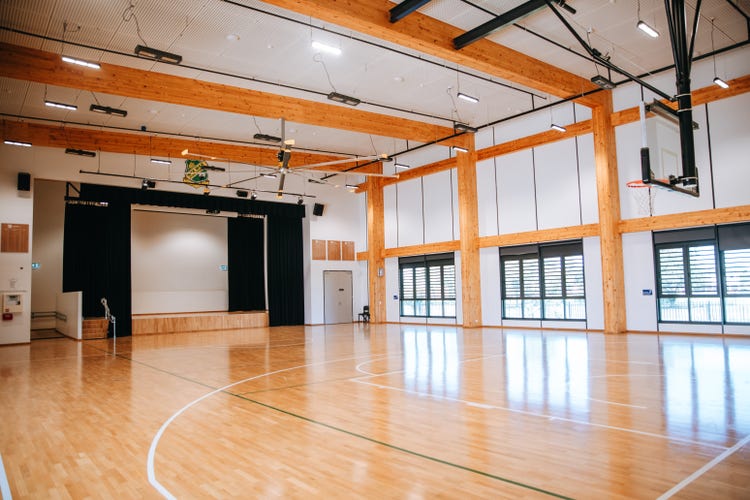 Photograph of interior of Wee Waa High School hall with polished timber flooring, half basketball court, high ceilings, large windows, and natural light