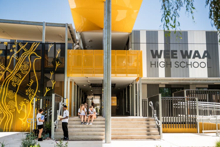 Photograph of Wee Waa High School building with students dressed in Wee Waa High School uniform sitting on steps and standing in front of Indigenous mural
