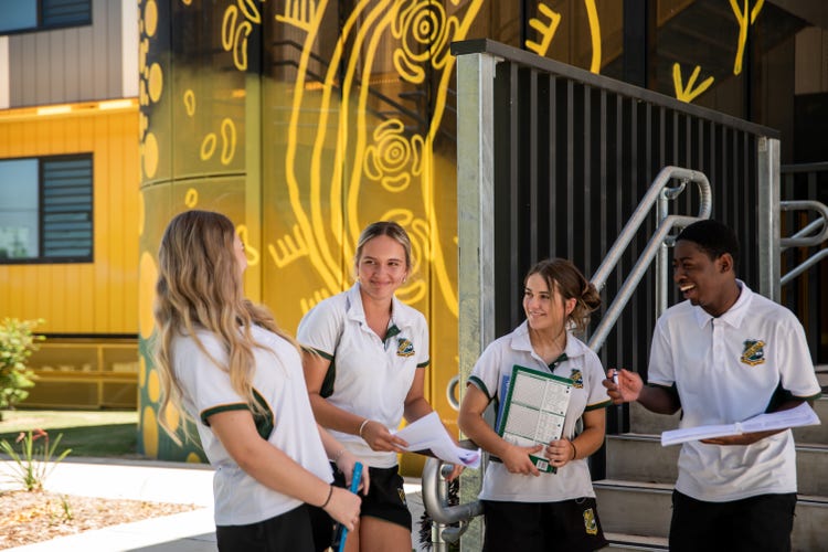 Photograph of students dressed in Wee Waa High School uniform smiling in front of Wee Waa High School Indigenous mural