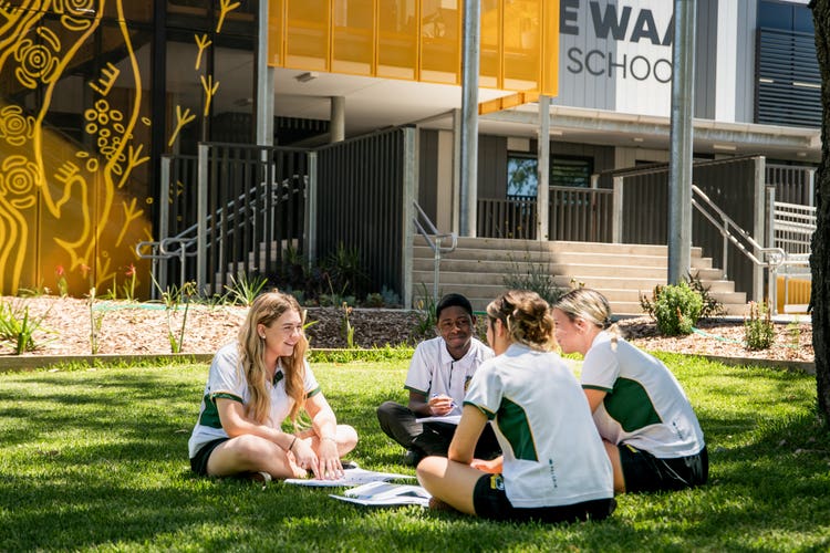 Photograph of students smiling dressed in Wee Waa High School uniform sitting in a circle on grassed area outside Wee Waa High School building