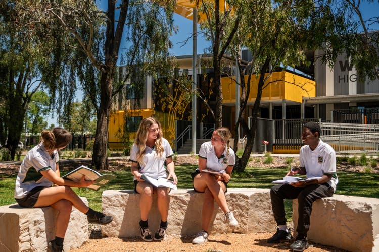 Photograph of students dressed in Wee Waa High School uniform smiling sitting at the yarning circle outside Wee Waa High School building surrounded by trees